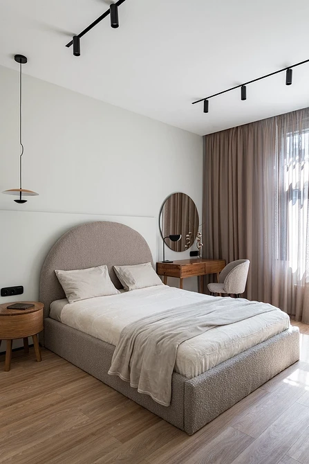 A modern bedroom with wooden floors and a beige bed.