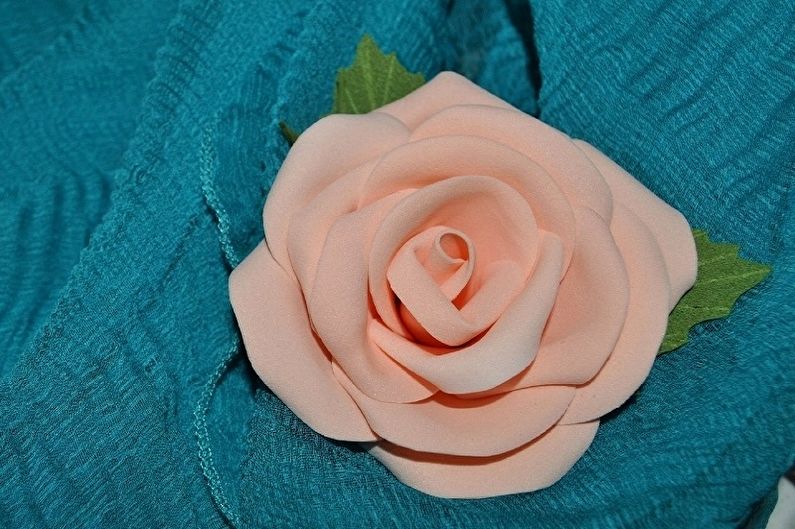 A peach rose brooch on a blue cloth.