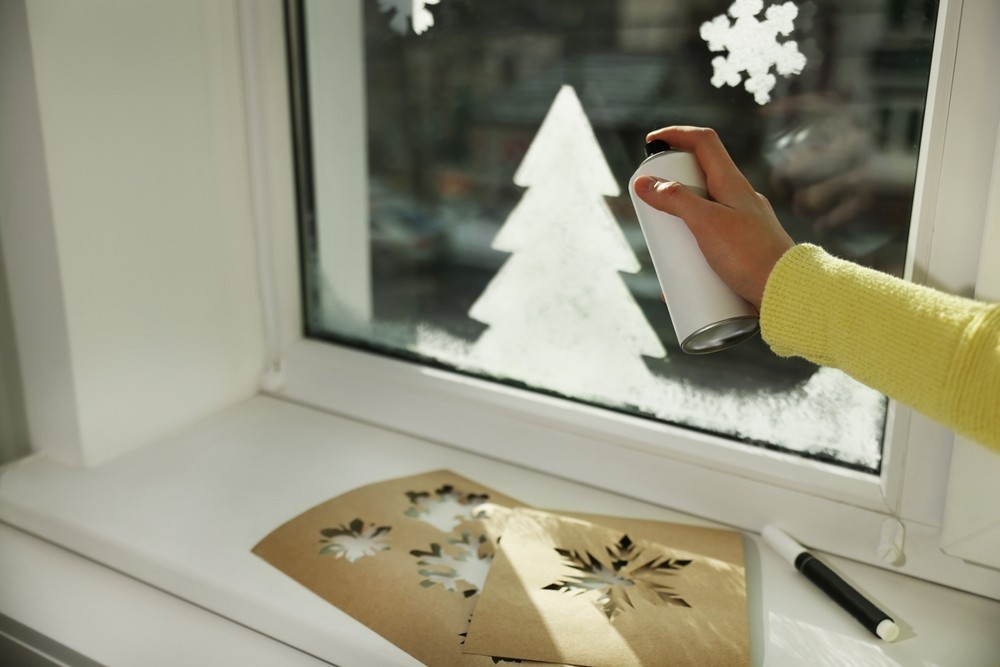 A person is spraying snowflakes on a window.