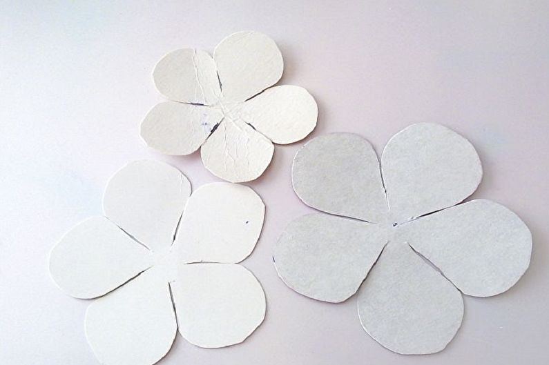 Three white paper flowers on a white surface.