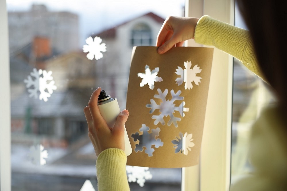 A woman is spraying snowflakes on a window.