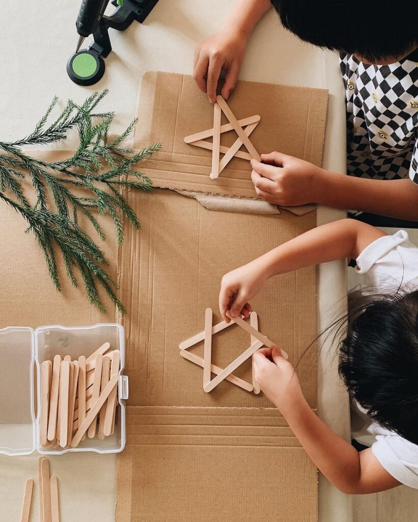 Two children are making popsicle star ornaments.