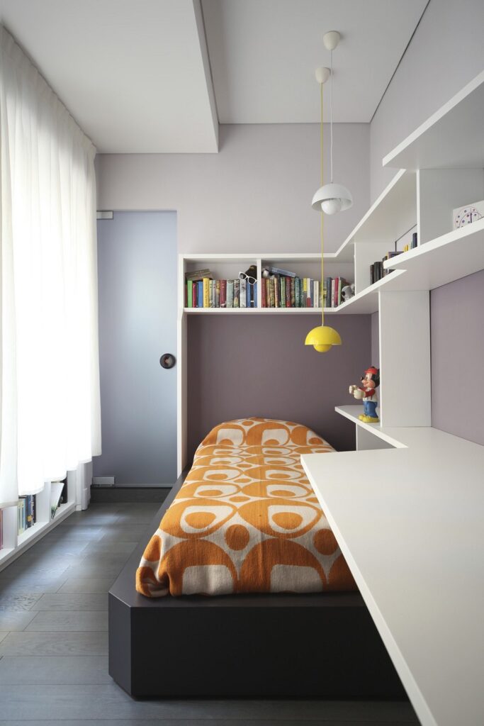 A bedroom with a bed, desk and bookshelves.