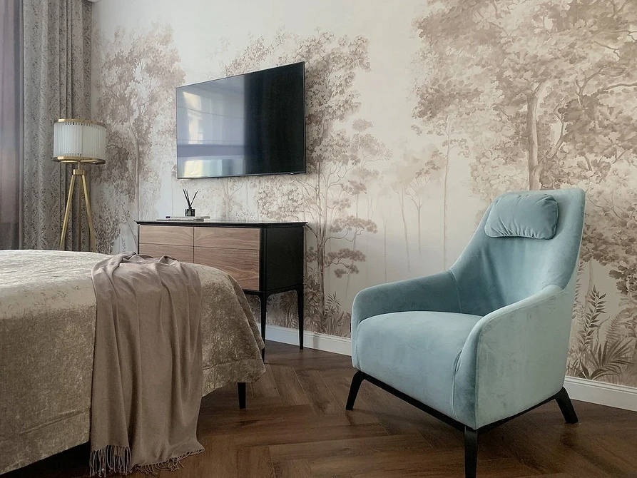 A bedroom with a blue chair and a tv on the wall.