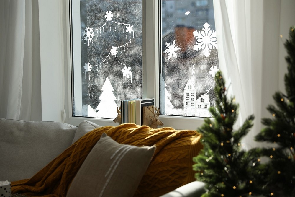 A living room with a christmas tree and snowflakes on the window.