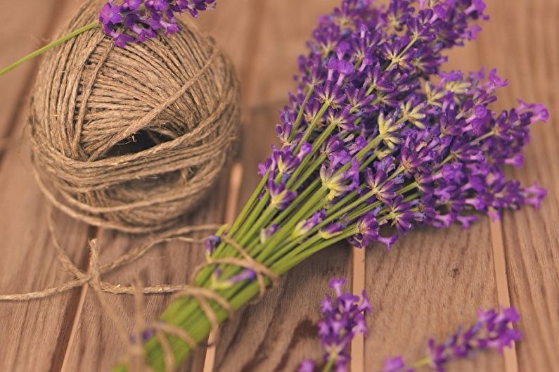 A bunch of lavender flowers and a spool of thread on a wooden table.