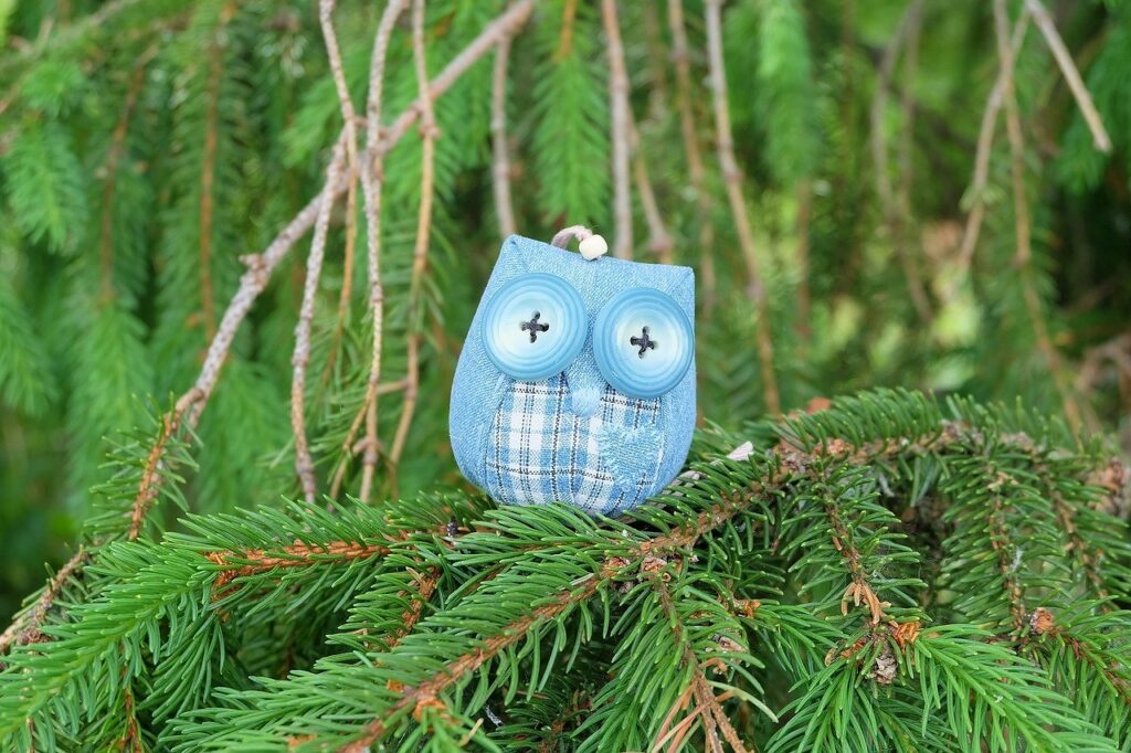 A blue owl sitting on a pine tree branch.