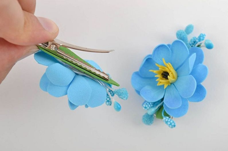 A person is holding a blue flower hair clip.