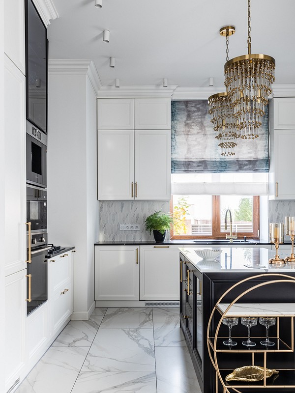 A white and gold kitchen with a chandelier.