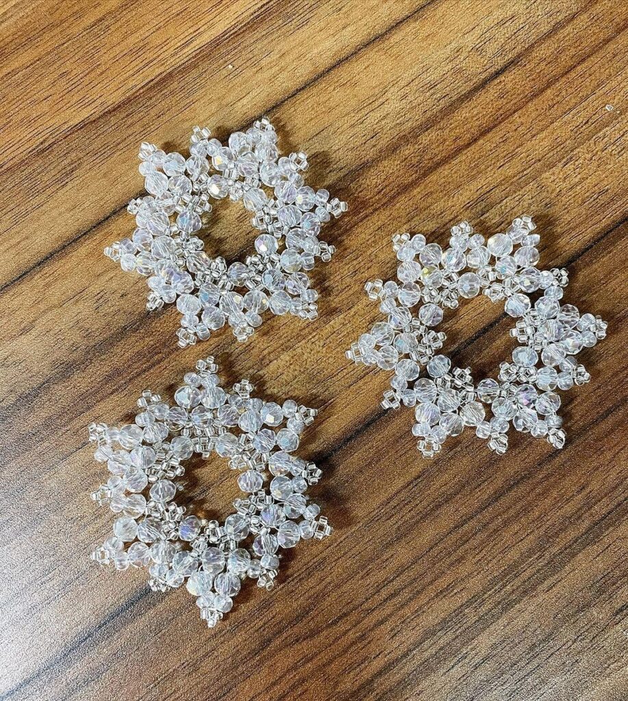 Three silver snowflake earrings on a wooden table.