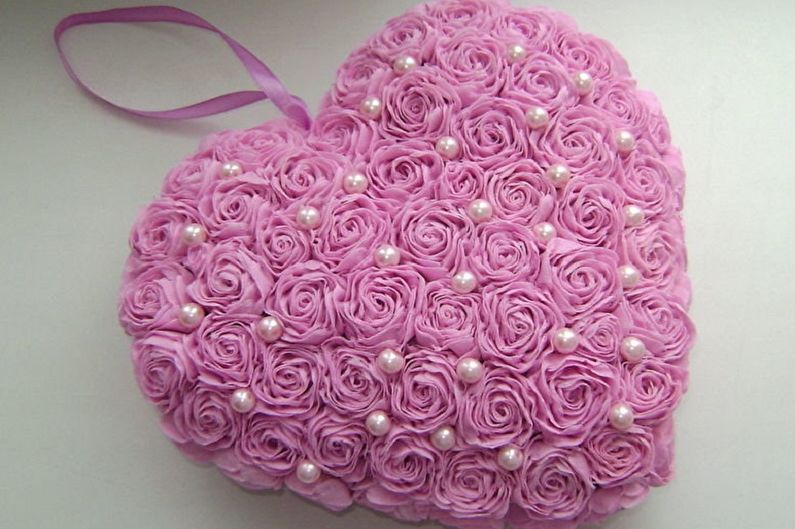 A pink heart shaped pillow with pearls and roses.