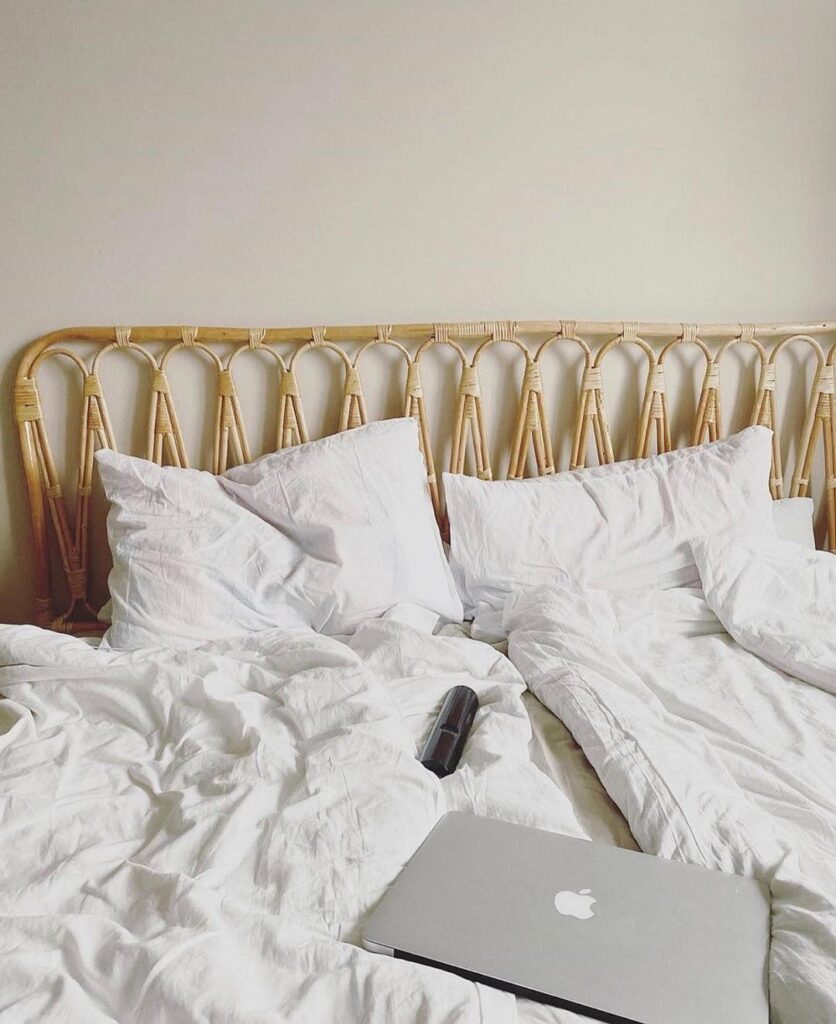 A bed with white sheets and a laptop on it.