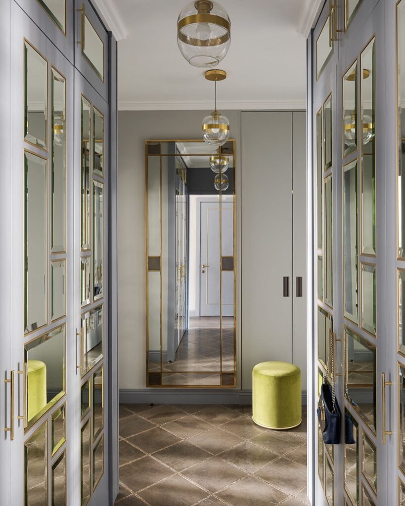 A hallway with gold mirrors and a green ottoman.