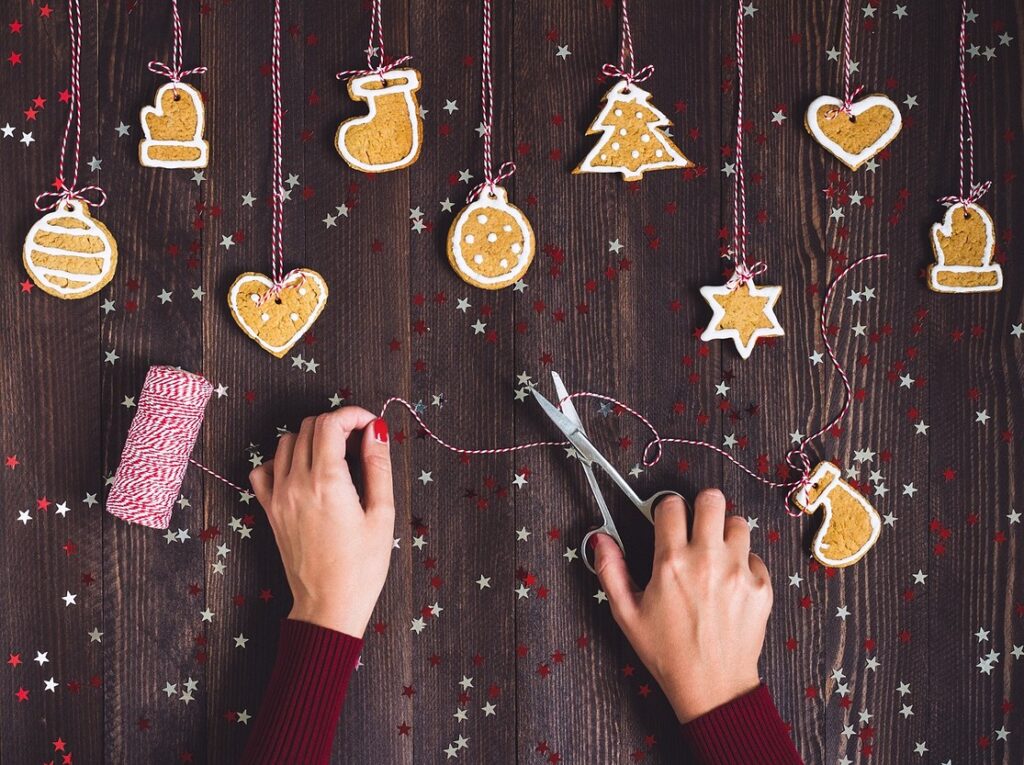 A woman is making christmas cookies with scissors on a wooden table.