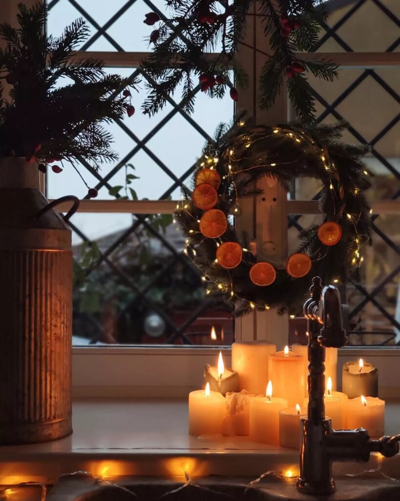 A christmas wreath and candles on a window sill.