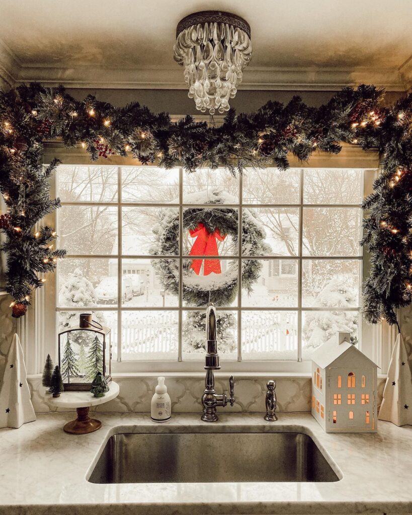 A christmas wreath hangs over a window in a kitchen.