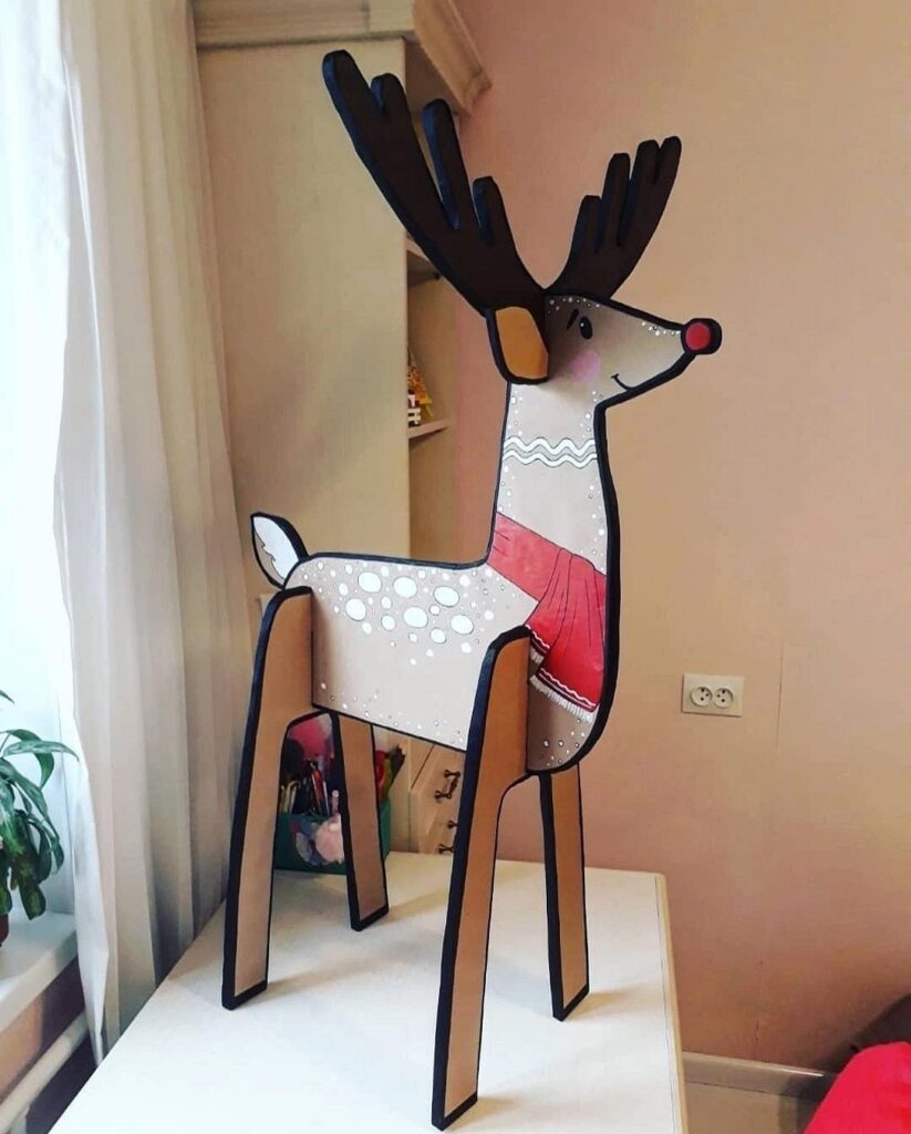 A paper reindeer standing on a table next to a bed.