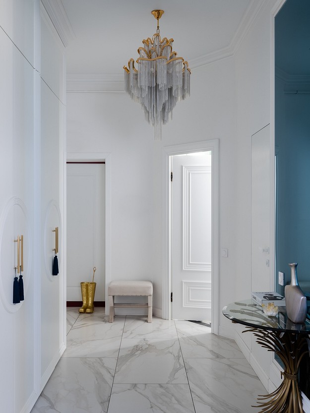 A white hallway with marble floors and a chandelier.