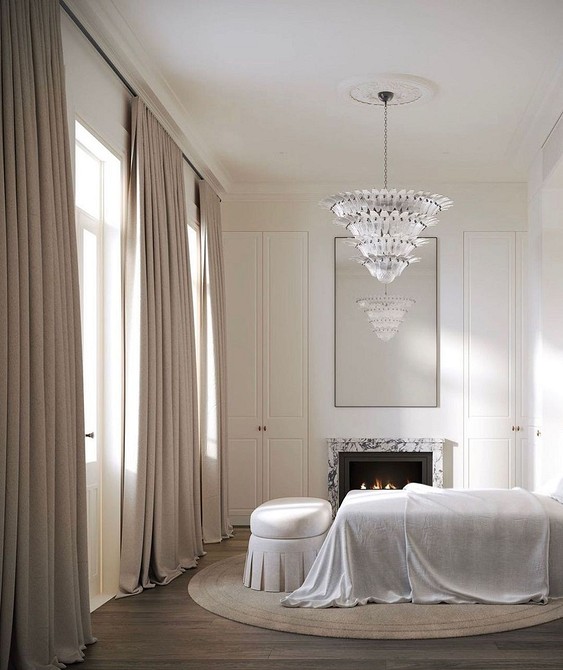 A white bedroom with a chandelier and a fireplace.