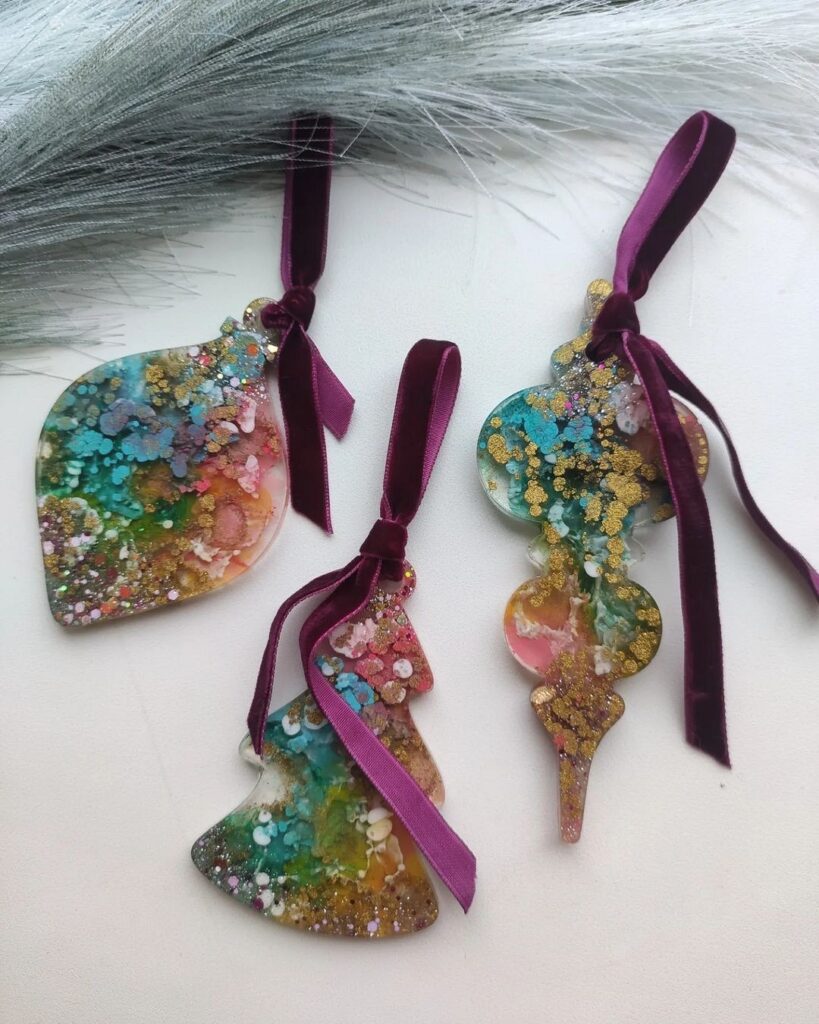 Three colorful christmas ornaments on a table with feathers.