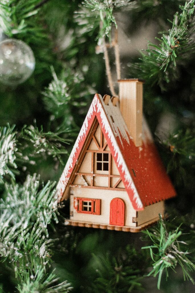 A wooden house ornament hangs on a christmas tree.