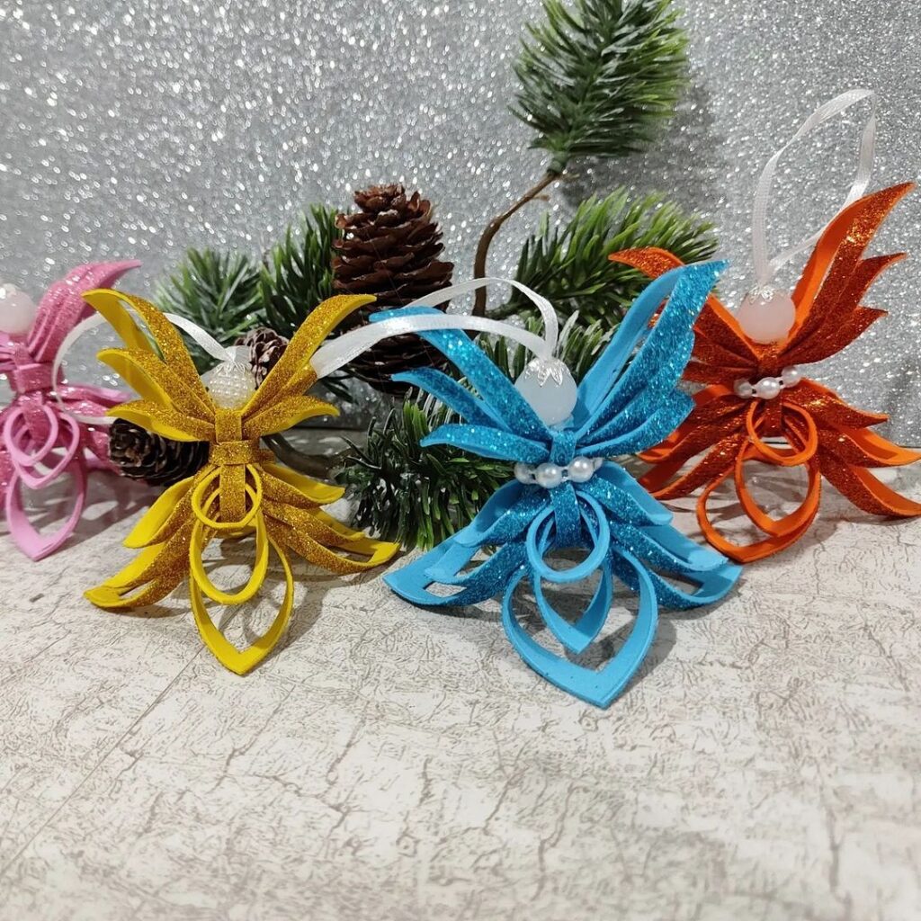 Four colorful paper angel ornaments with pine cones and pine needles.