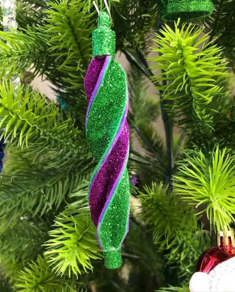 A purple and green ornament hangs on a christmas tree.