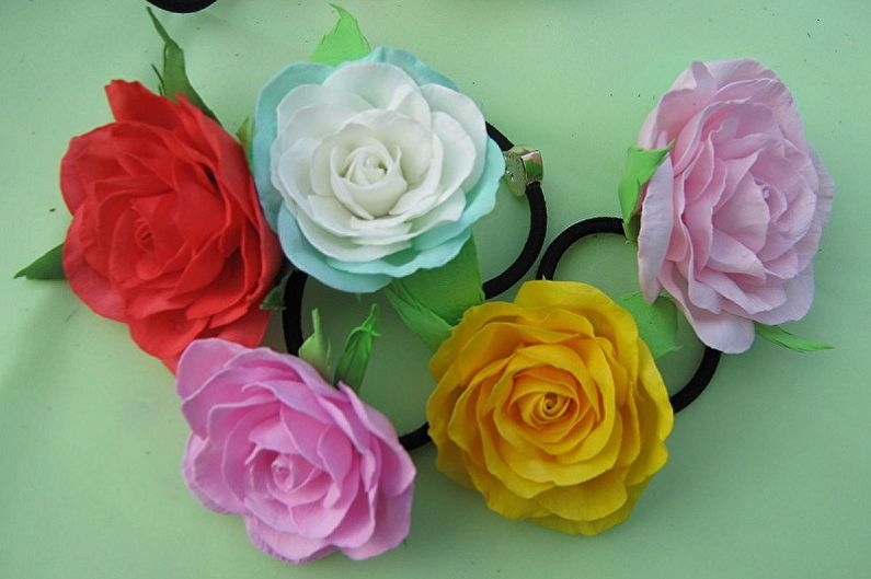 Four different colored paper roses are arranged on a green surface.