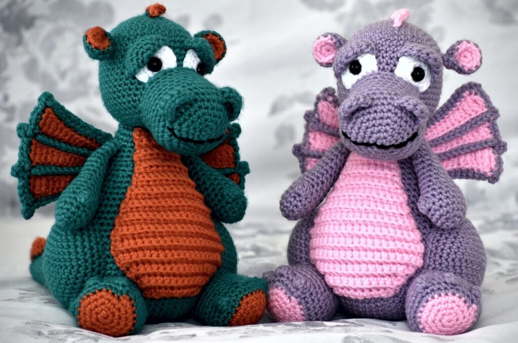 Two crocheted dragons sitting on a bed.