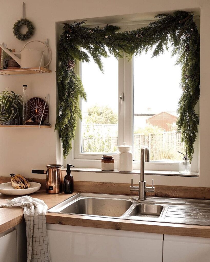 A kitchen with a christmas garland hanging over the sink.