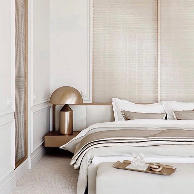 A white and beige bedroom with a bed and a lamp.