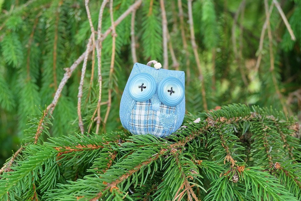 A blue owl ornament is sitting on a pine tree branch.