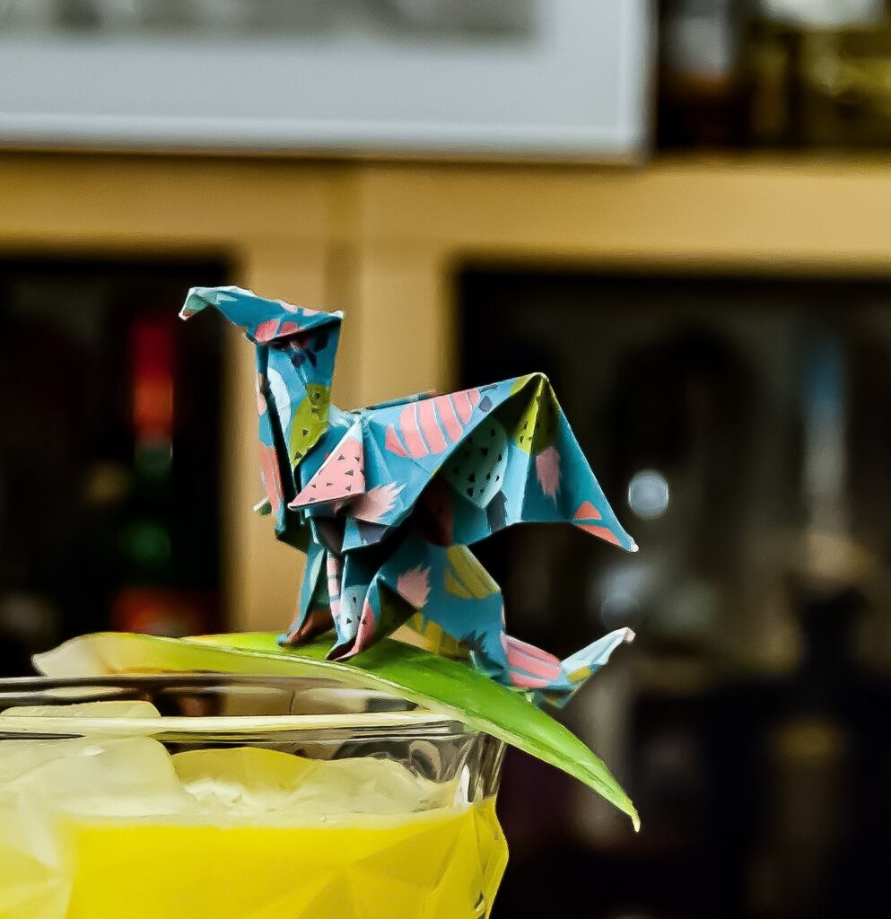 An origami dragon sits on top of a drink.