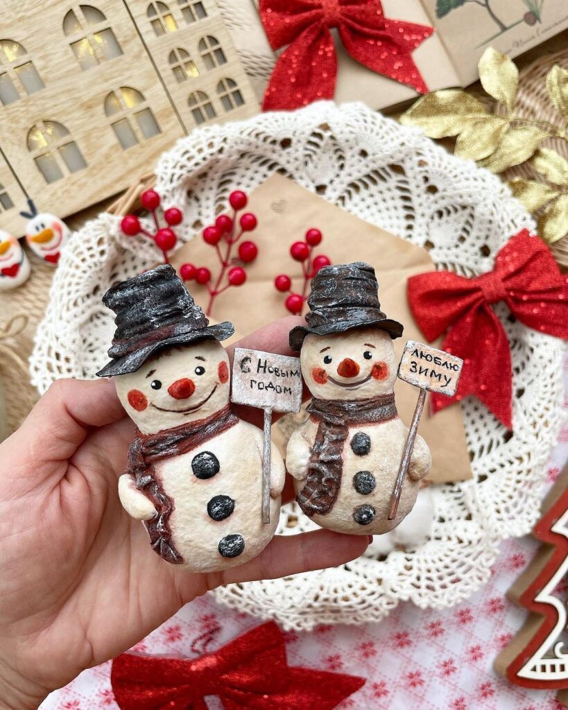 A person holding two snowmen figurines on a table.