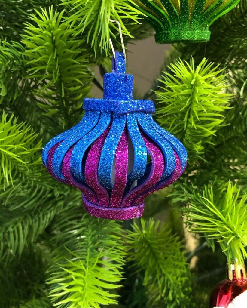 A blue, pink and purple ornament hangs on a christmas tree.